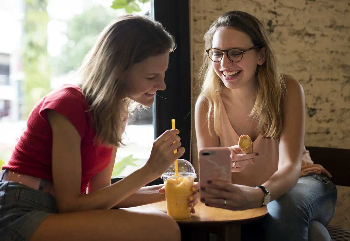 Two students enjoying a snack while looking at phone